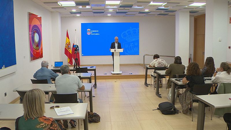 Señor Silva, con traje y barba, habla en un evento oficial del "GOBIERNO de CANTABRIA" ante una audiencia atenta. Banderas de España y Cantabria presentes.