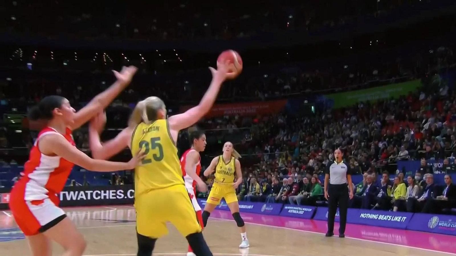 Jugadora australiana Kristy Wallace (25) en el aire con el balón, Sami Whitcomb (7) cerca. Árbitra atenta. Vallas publicitarias: "WORLD CUP AUSTRALIA 2022".