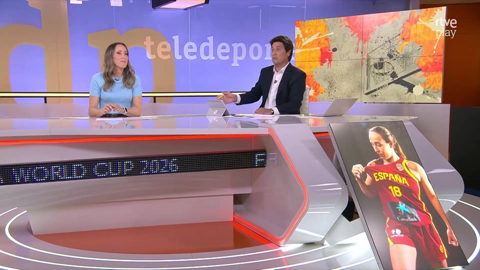 Plató de televisión con presentadores Lourdes García Campos y Marcos López, pantalla "teledeporte" y "rtve play", texto "WORLD CUP 2026" y jugadora de baloncesto.