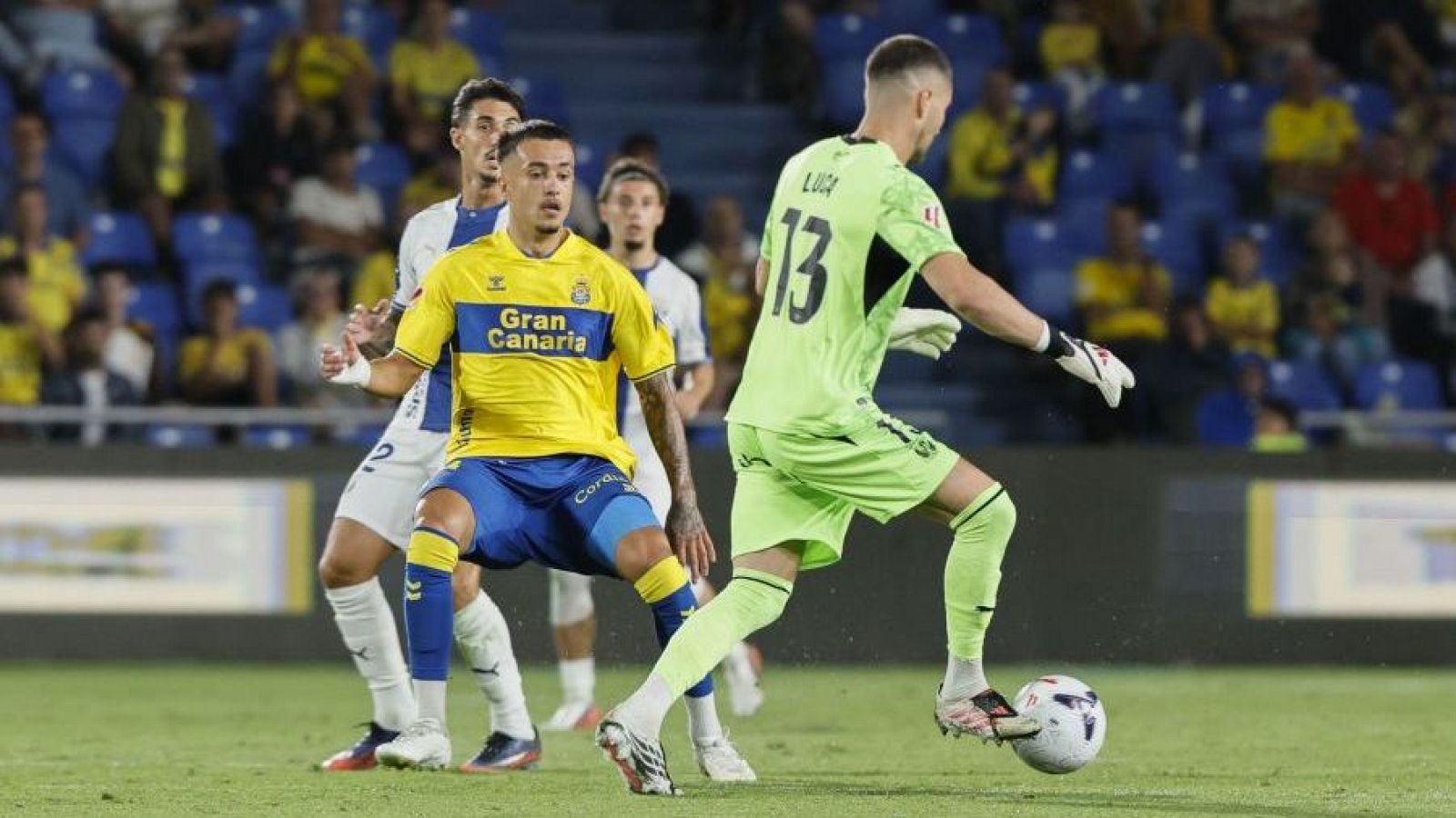 Jonathan Viera (UD Las Palmas) y Luca Zidane (portero) en acción. El balón está a los pies de Zidane, en un partido nocturno en un estadio lleno.