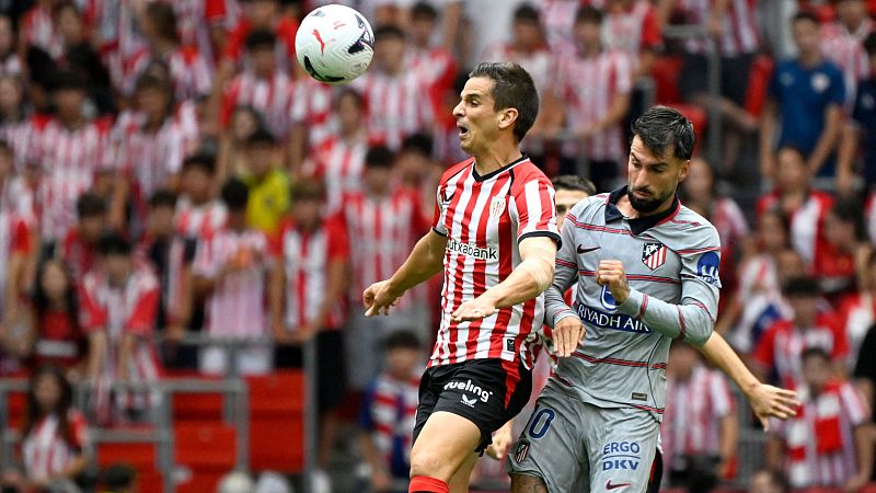 Raúl García (Athletic Club) y Antoine Griezmann (Atlético de Madrid) luchan por el balón en un partido de Primera División. El balón está en el aire, con público al fondo.