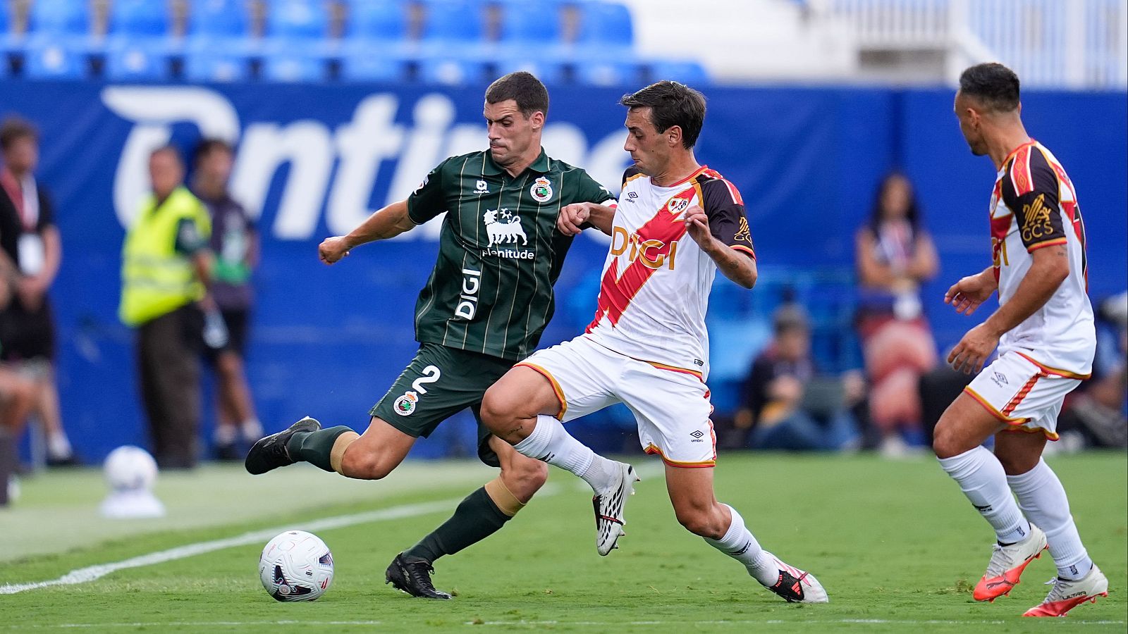 Álvaro Mantilla (Real Racing Club) y Pedro Díaz (Rayo Vallecano) disputan el balón en un partido de fútbol. Se aprecian detalles de sus equipaciones y la intensidad de la jugada.