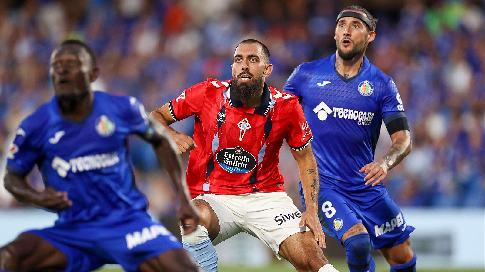 Iago Aspas y Nemanja Maksimović, junto a otro jugador del Getafe, se concentran intensamente en un partido de fútbol, siguiendo la trayectoria de la acción en el aire.
