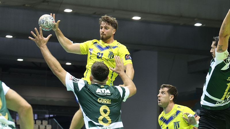 Jugador con dorsal 31 en amarillo salta con bal�n "SELECT". Defensor "GURRI" (dorsal 8) en verde intenta bloquear. Acci�n de balonmano en pabell�n.