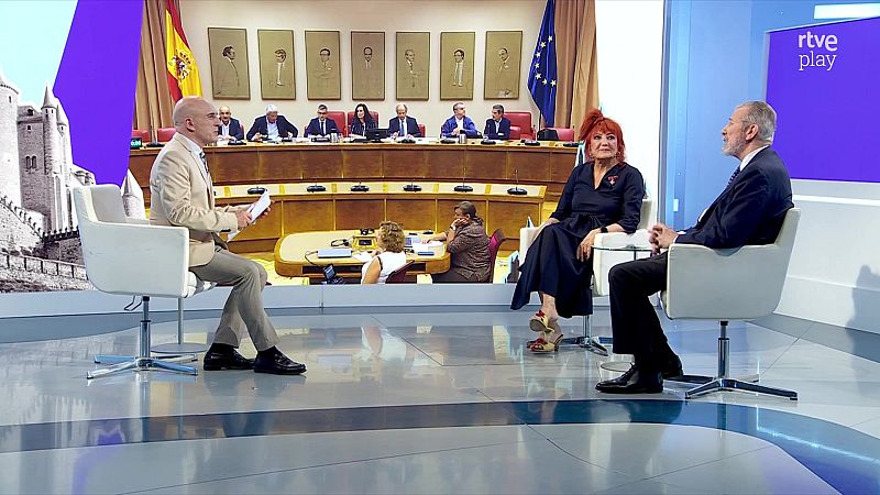 Rosa Montero y Juan Mayorga son entrevistados por un presentador en un plat� de "rtve play" con fondo de hemiciclo, banderas de Espa�a y UE, y un castillo medieval.