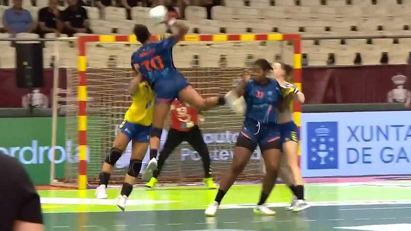 Jugadora 70 de azul salta para lanzar a porter�a en partido de balonmano. Defensoras amarillas y portera roja intentan parar el tiro. Vallas de Iberdrola y Xunta de Galicia visibles.