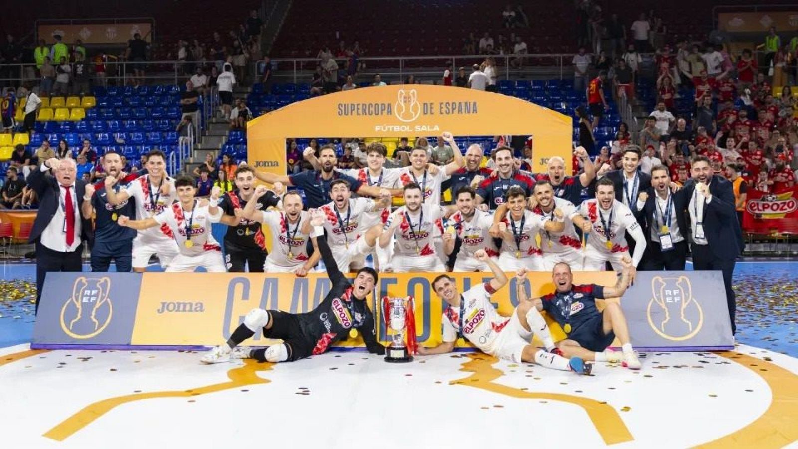 Jugadores de ElPozo Murcia Costa Cálida celebran la Supercopa de España de Fútbol Sala con el trofeo, medallas y el presidente José María Albarracín y el entrenador Javi Rodríguez. Confeti y público en gradas.