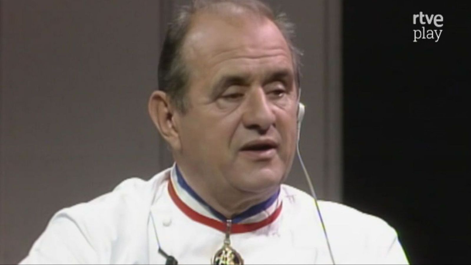 Primer plano de Paul Bocuse, chef francés, con chaqueta blanca, medalla dorada y auricular. Logo "rtve play" visible.