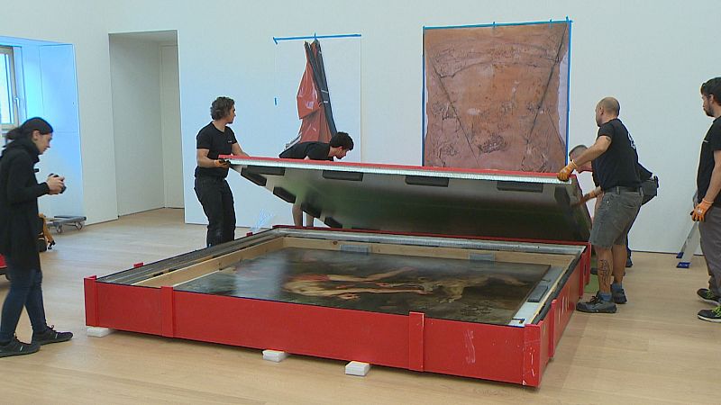 Desembalaje de una obra de arte clásica de un cajón rojo en una sala de exposiciones, con varias personas involucradas en el proceso.