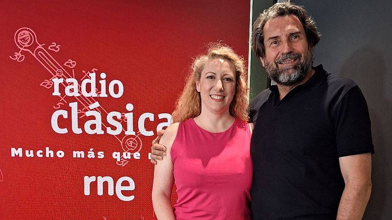 Saioa Hernández y Arturo Reverter sonríen frente a un fondo rojo con "radio clásica" y "rne". Ella lleva un vestido fucsia, él un polo negro y la abraza.
