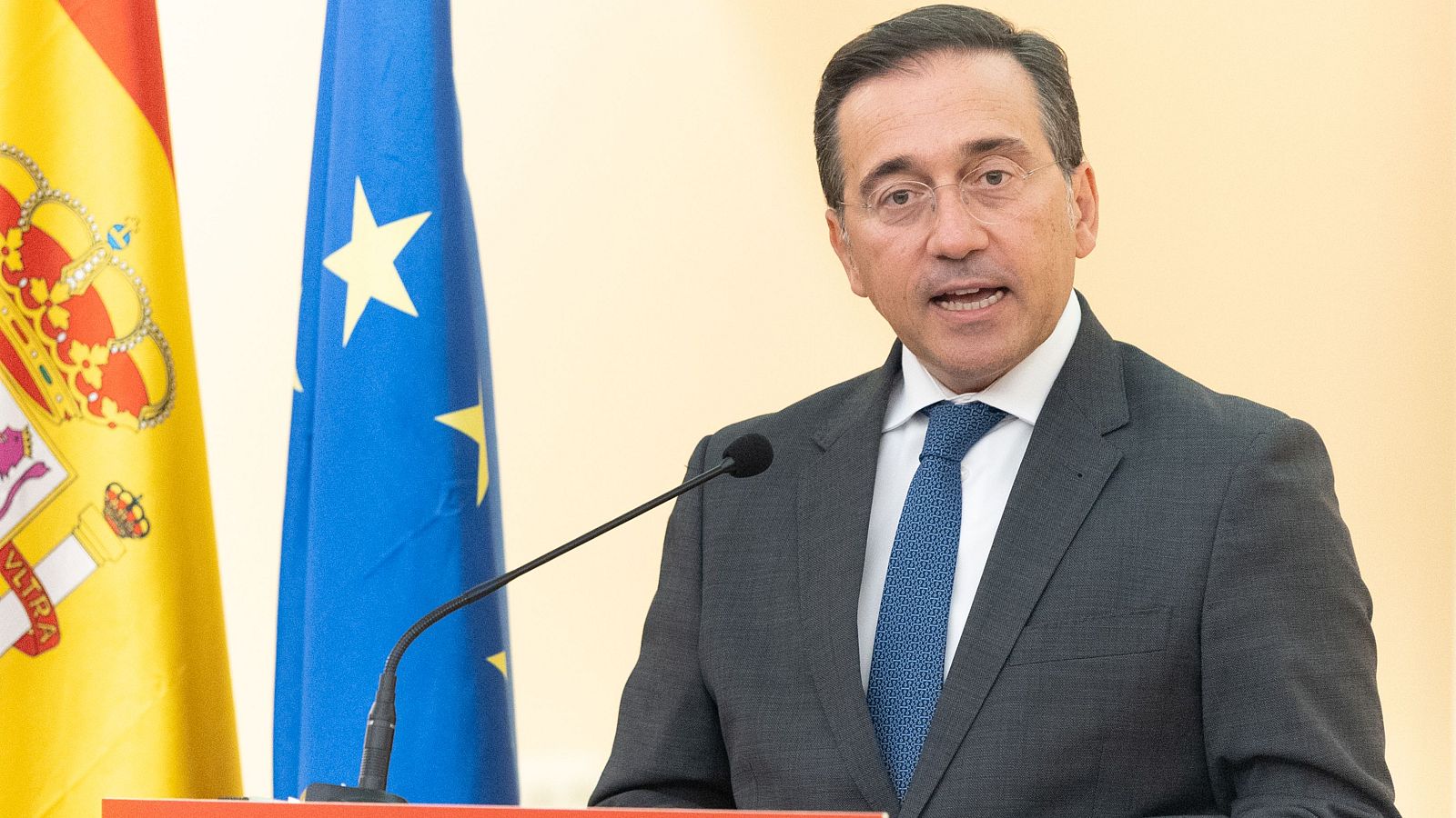 José Manuel Albares, Ministro de Asuntos Exteriores, habla en un evento oficial con las banderas de España y la UE de fondo.
