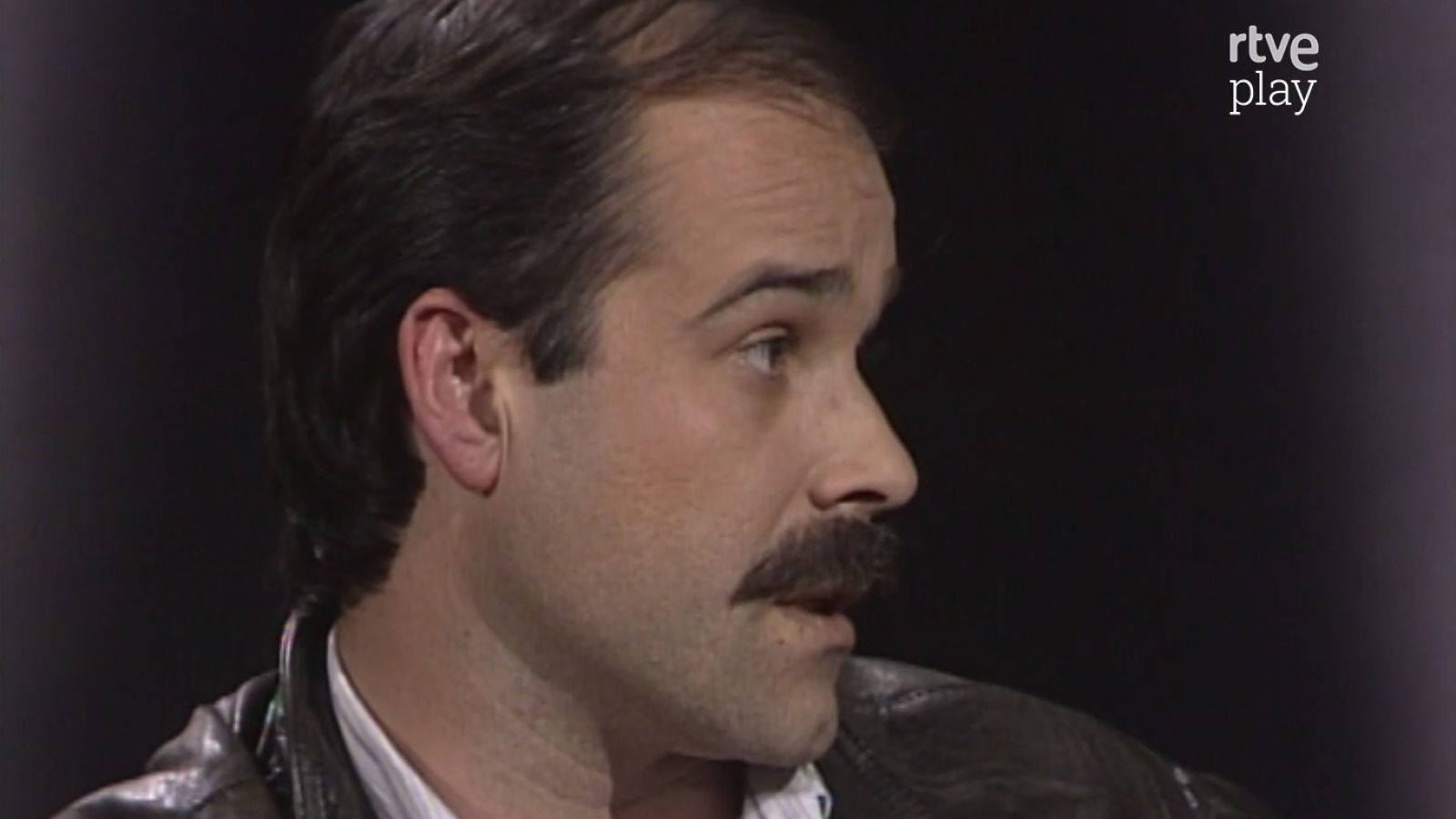 Antonio Resines de perfil, con bigote y chaqueta oscura. Fondo negro con logo 'rtve play'.