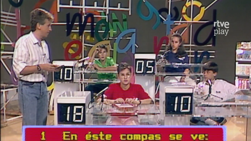 Ramón García presenta un concurso con cuatro jóvenes concursantes en un plató colorido con el logo de rtve play. Una banda roja inferior muestra "1 En éste compas se ve:".