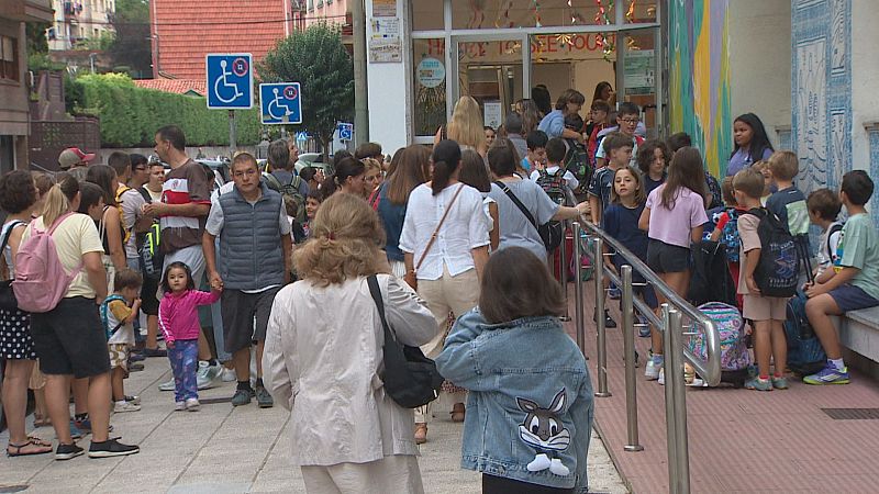 Alumnos y adultos entran a un colegio en el primer día de clases, con un mural vibrante y señales de accesibilidad en la entrada.