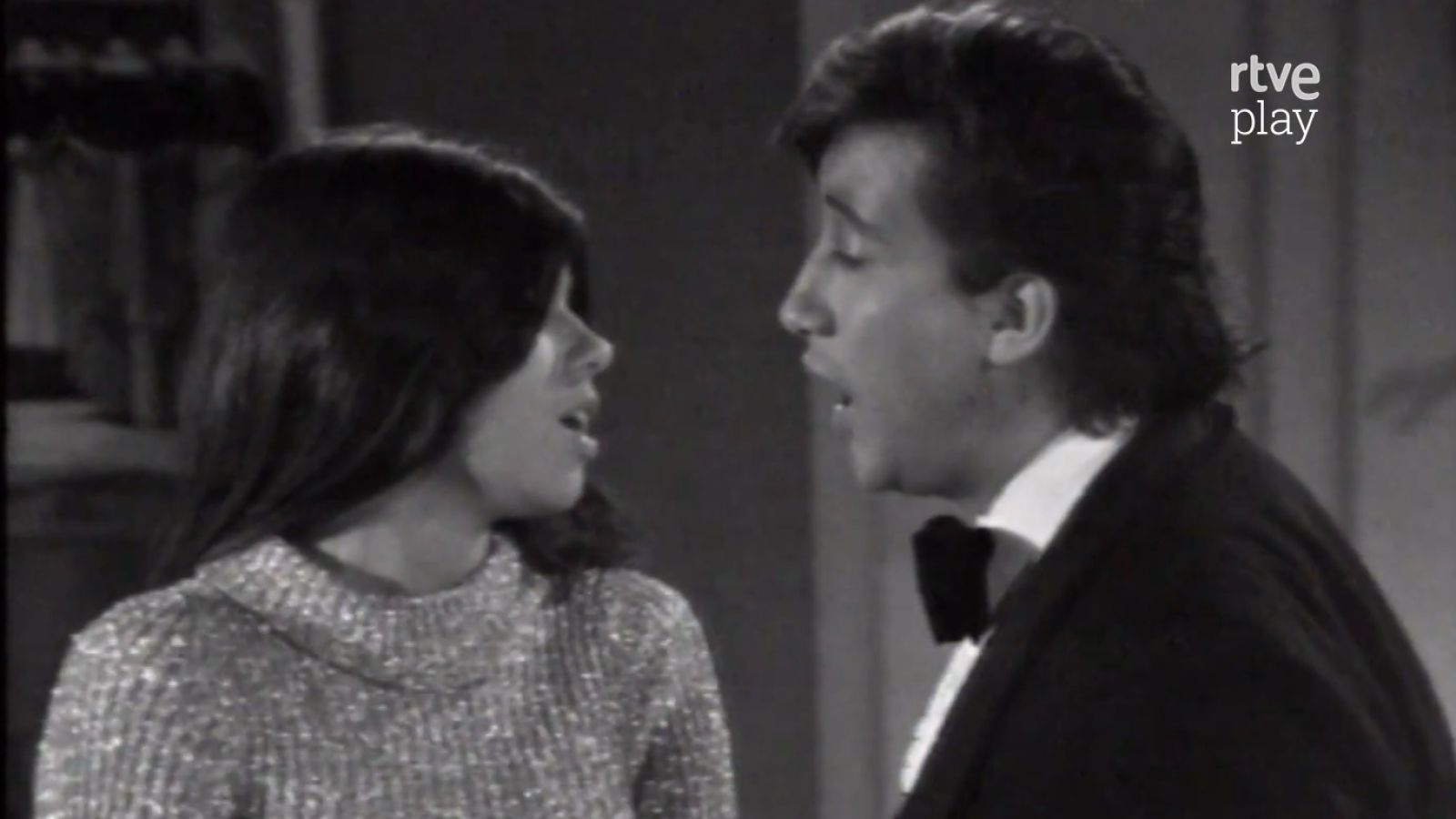 Primer plano en blanco y negro de Jeanette y un hombre cantando juntos, con "rtve play" en la esquina superior derecha. Estilo de mediados/finales del siglo XX.