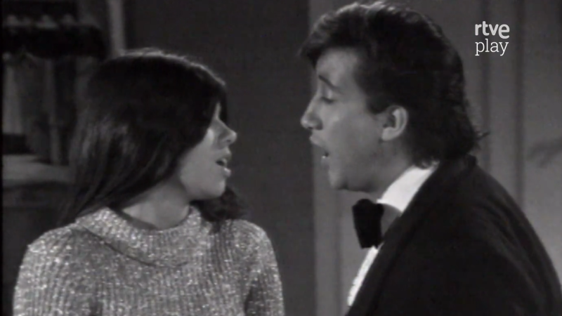 Primer plano en blanco y negro de Jeanette y un hombre cantando juntos, con "rtve play" en la esquina superior derecha. Estilo de mediados/finales del siglo XX.