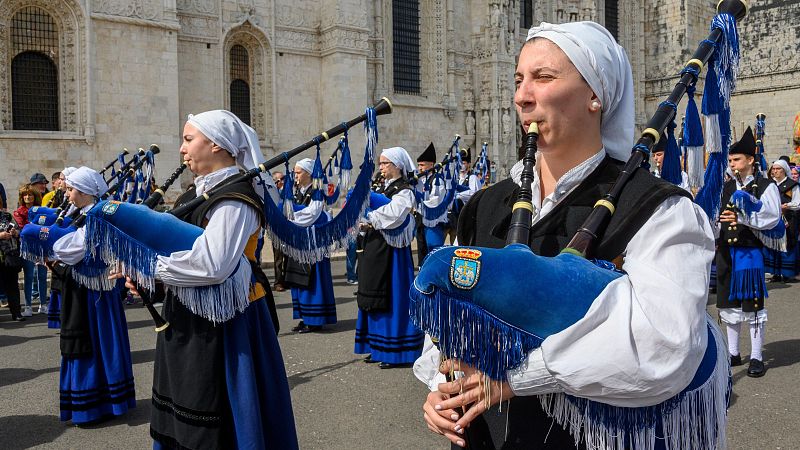 Mujer tocando una gaita azul con el escudo de Oviedo, rodeada por la Real Banda de Gaitas 'Ciudad de Oviedo' frente al Monasterio de los Jerónimos en Lisboa.
