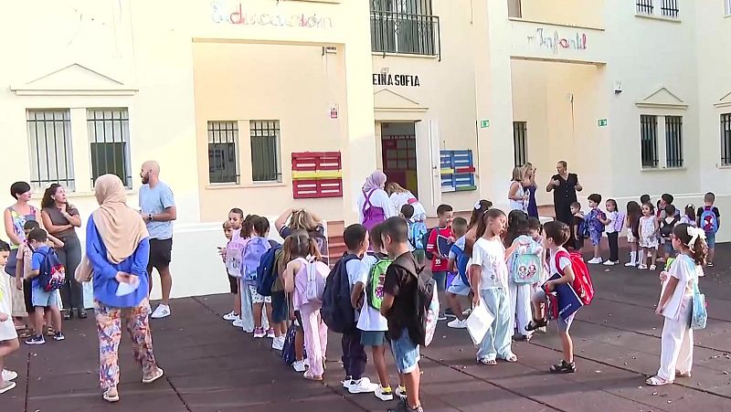 Niños y adultos llegan al CEIP Reina Sofía en Ceuta para el inicio del curso escolar infantil, con el cartel "Infantil" visible en el edificio.