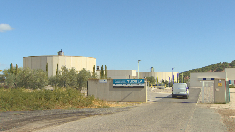 Vista exterior de la Depuradora de Aguas Residuales de Tudela con furgoneta blanca entrando, cartel informativo y vegetación.