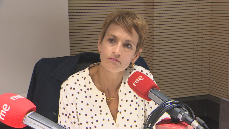 María Chivite, Presidenta del Gobierno de Navarra, posa con micrófonos de Radio Nacional de España. Lleva blusa blanca con lunares y joyas doradas.