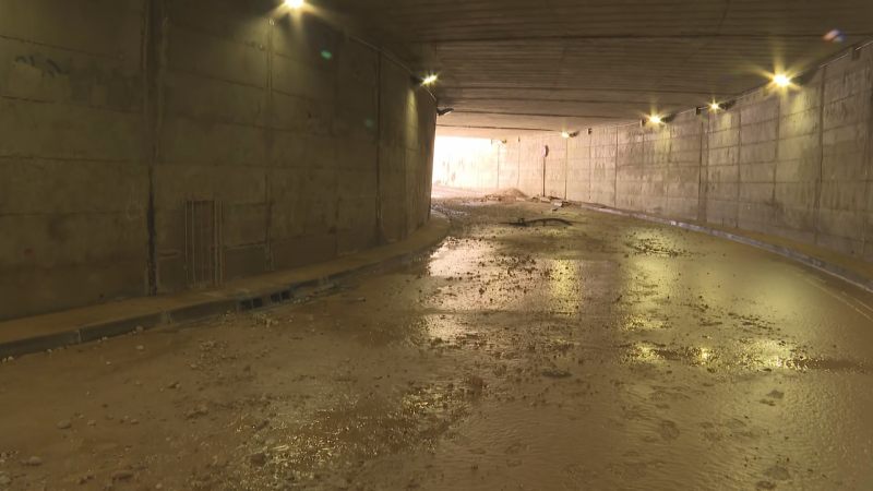 Túnel de hormigón inundado con agua, barro y escombros. Luces en el techo y una salida brillante al fondo.