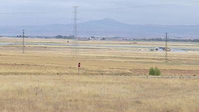 Paisaje rural con campo seco, se�al de prohibido el paso, torres el�ctricas y monta�as brumosas bajo cielo cubierto.