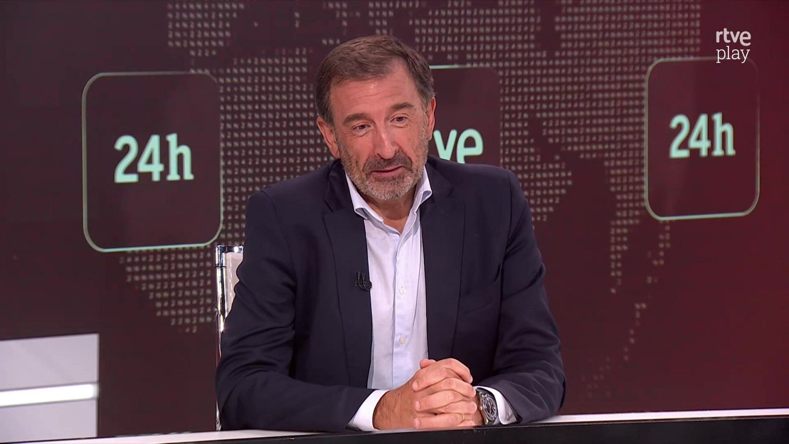 Carlos Franganillo, periodista, en estudio de TV con logo "rtve play" y "24h" en el fondo. Viste traje oscuro y camisa azul pálido. Expresión seria.