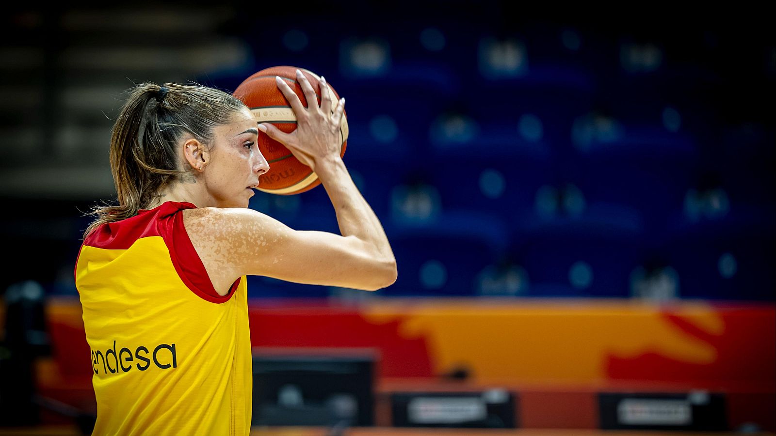 Mariona Ortiz, jugadora de baloncesto, posa de perfil con un balón, vistiendo camiseta amarilla con detalles rojos y logo "Endesa".