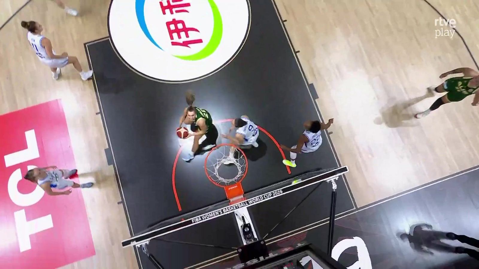 Vista aérea de un partido de baloncesto femenino. Jugadora con balón bajo el aro, rodeada de defensoras. Se aprecian logos de FIBA, TCL y rtve play.