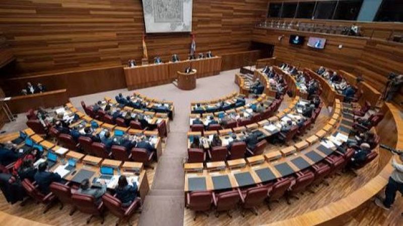 Vista aérea del hemiciclo de las Cortes de Castilla y León en pleno ordinario. Diputados en sus escaños, mesa presidencial con banderas, orador en el podio y pantallas informativas. Presencia de medios de comunicación.