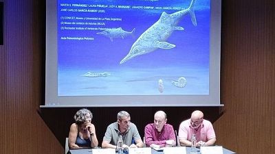 Presentaci�n cient�fica con paleont�logos en una sala de conferencias, mostrando un ictiosaurio y f�siles en pantalla. Se identifican a Laura Pi�uela, Jos� Carlos Garc�a-Ramos y Angel Garc�a P�rez.