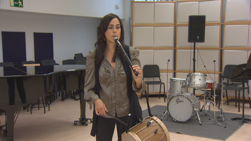Mujer tocando txistu y tamboril en estudio musical con piano, batería Gretsch y paneles acústicos.