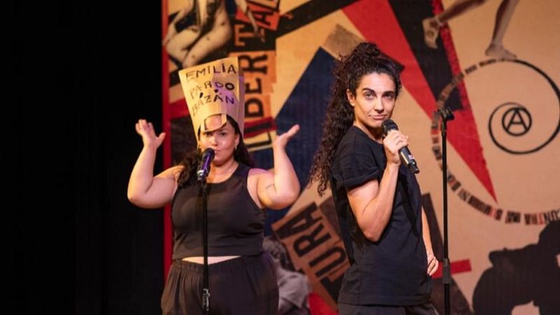 Dos mujeres actúan en un escenario. Una lleva un sombrero con "EMILIA PARDO BAZÁN". El fondo muestra "LIBERTAD", "CULTURA" y un símbolo anarquista.
