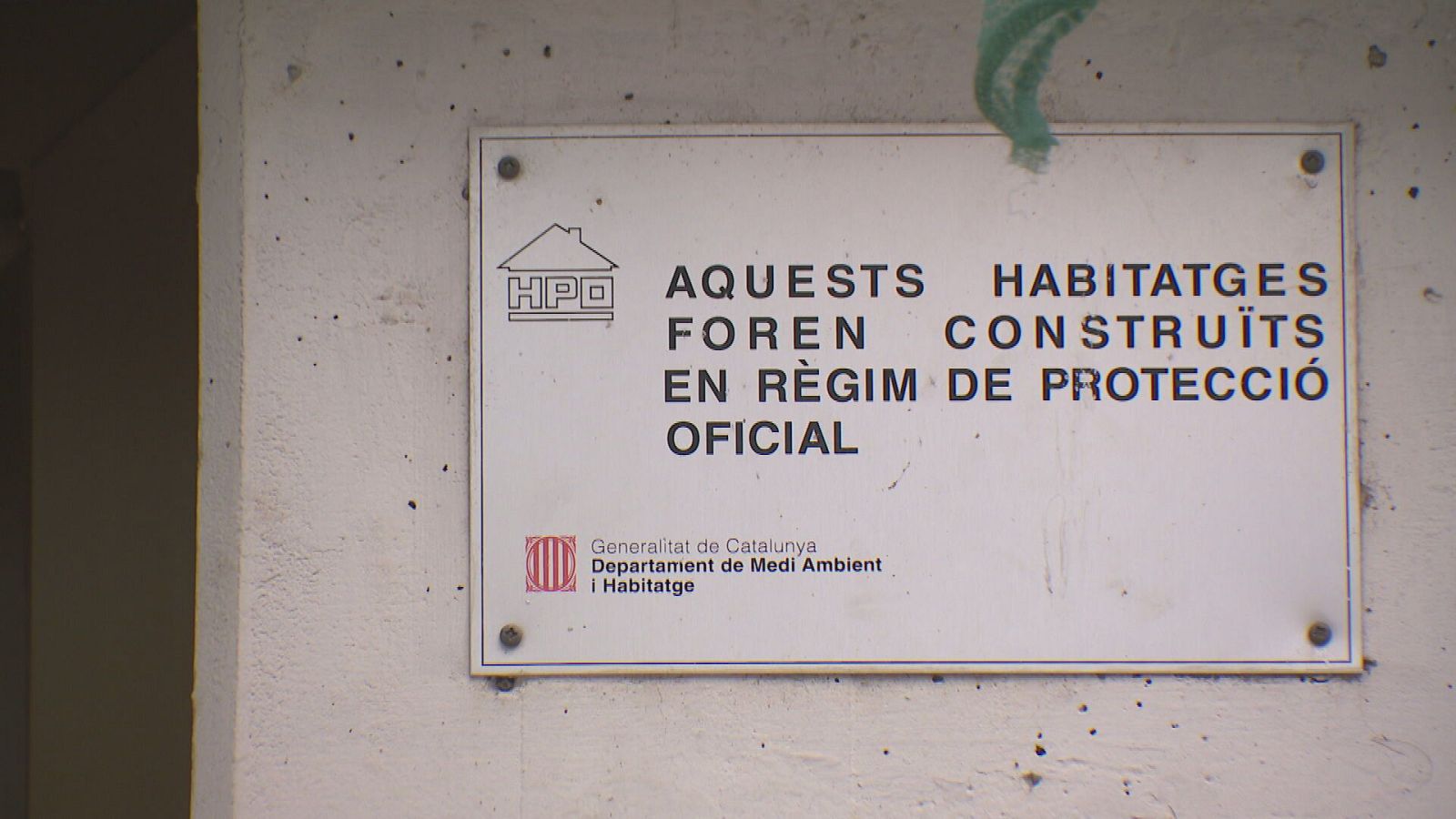 Cartel blanco sobre pared gris con texto en catalán sobre viviendas de protección oficial, logotipo HPO y escudo de la Generalitat de Catalunya.