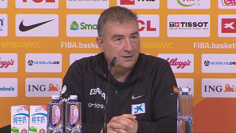 Entrenador de baloncesto español Miguel Méndez en rueda de prensa, con logos de Nike, CaixaBank y bandera de España. Fondo con patrocinadores Tissot y FIBA.