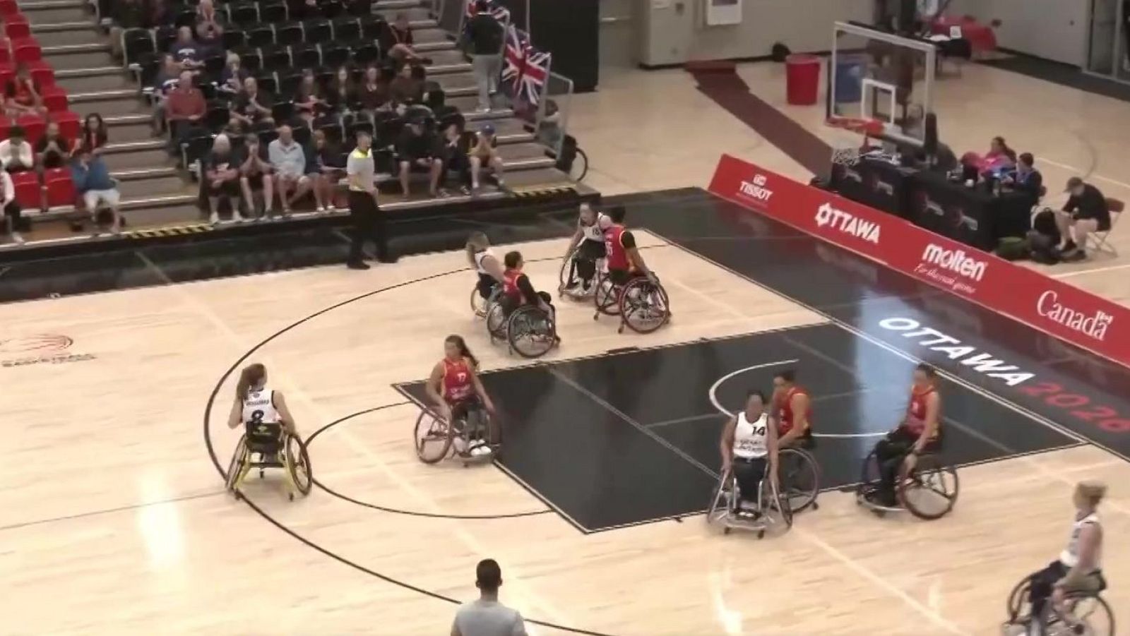 Vista aérea de un partido de baloncesto en silla de ruedas con jugadores en acción, gradas llenas y un banner publicitario de TISSOT y OTTAWA 2026.