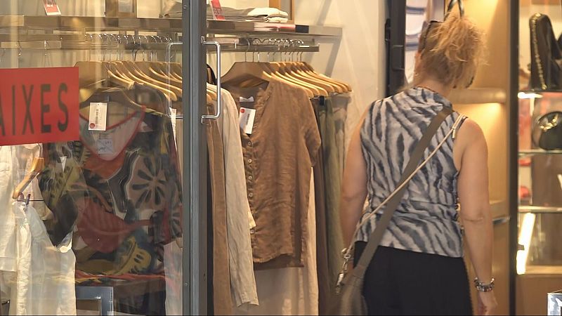 Mujer de espaldas con camiseta de cebra y bolso cruzado, frente a un escaparate con ropa y un cartel de "AIXES" (posiblemente "REBAIXES").