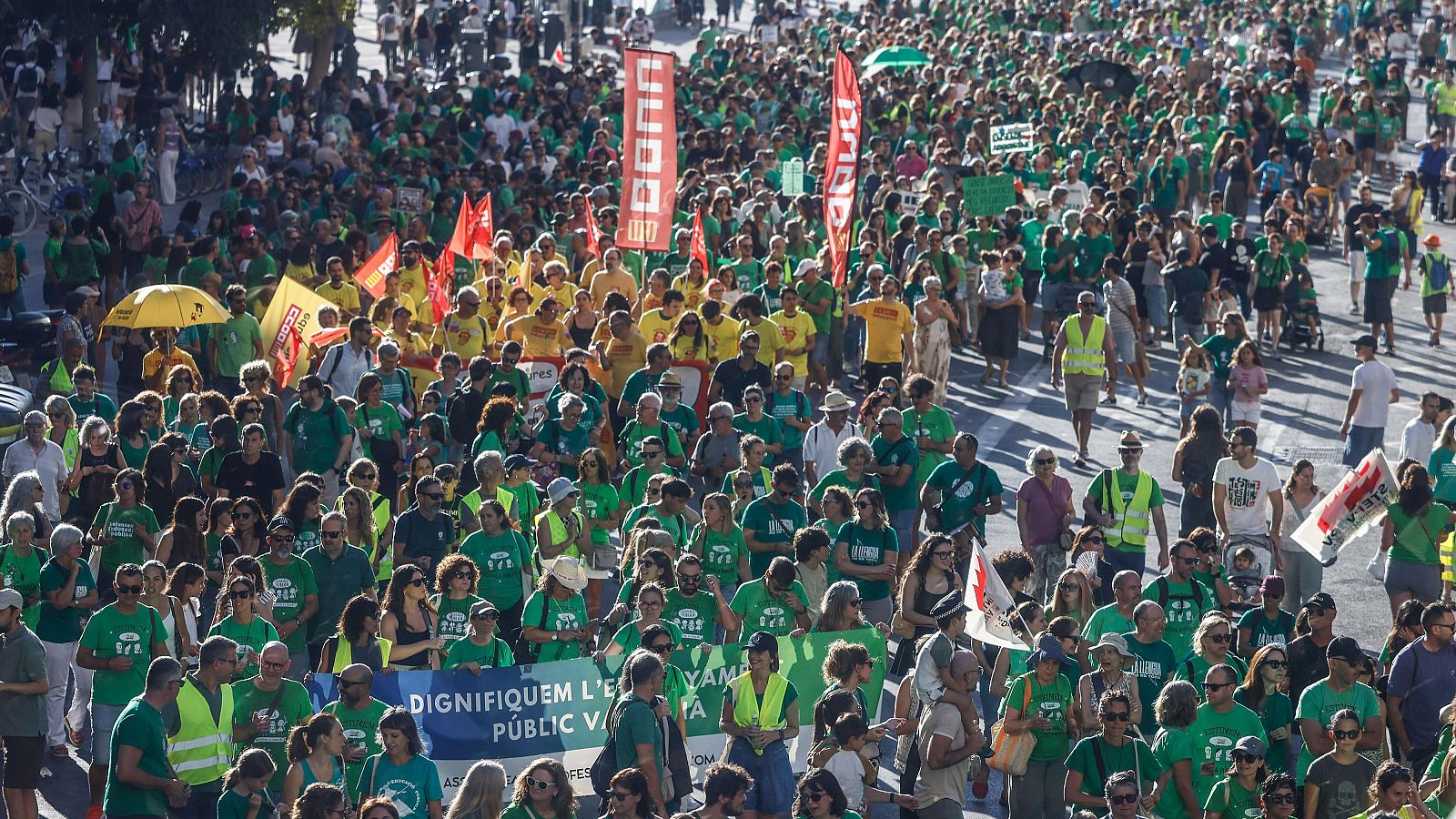 Manifestación masiva por la escuela pública con pancartas en catalán y banderas de sindicatos como CGT, CCOO y UGT.