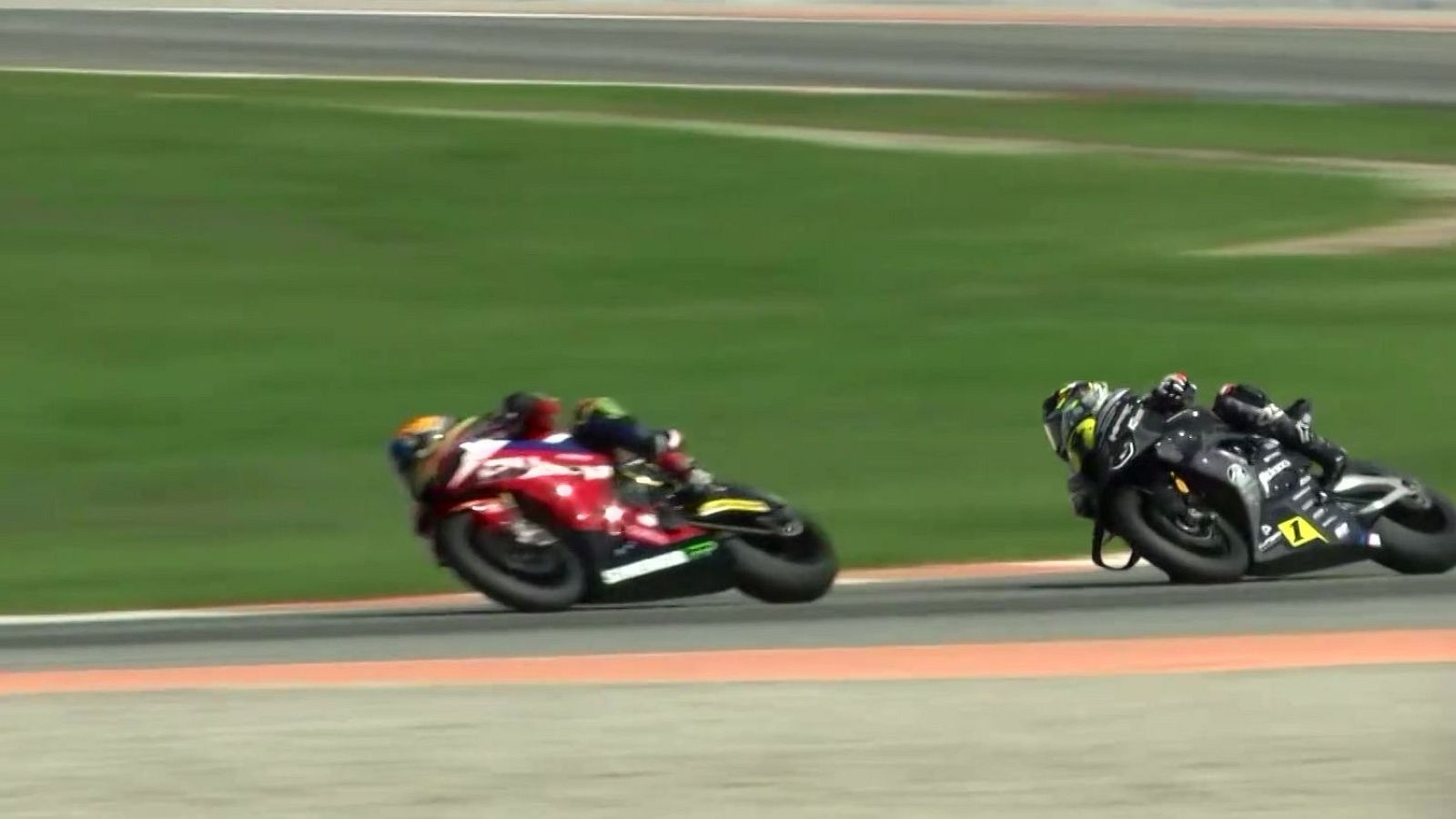 Dos pilotos de motociclismo en plena curva, uno en moto roja y otro en moto negra con el número 7 amarillo, inclinados a alta velocidad en un circuito.