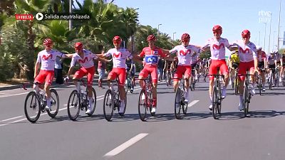 Ciclistas del equipo Movistar en un evento, con el logo 'LA VUELTA' y 'rtve play' visibles. El ciclista 3 destaca con maillot rojo.