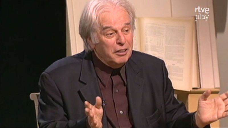 Alejandro Jodorowsky, con traje oscuro y camisa burdeos, gesticula mientras habla. Fondo con libro abierto y logo "rtve play".