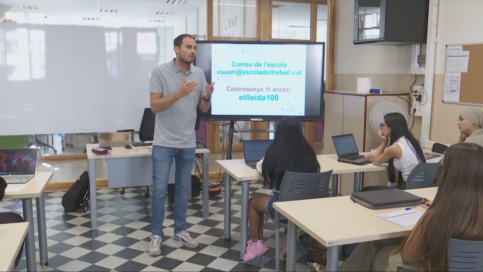 Instructor imparte clase sobre correo electrónico a estudiantes femeninas. Pantalla muestra "Correu de l'escola" y contraseña "etlleida100".