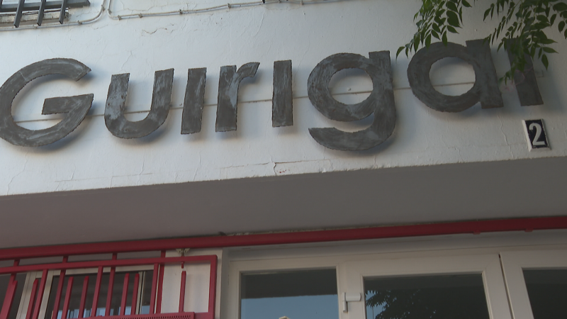 Fachada de edificio con letrero "Guirigai" y número "2". Estructura roja y vegetación visible.
