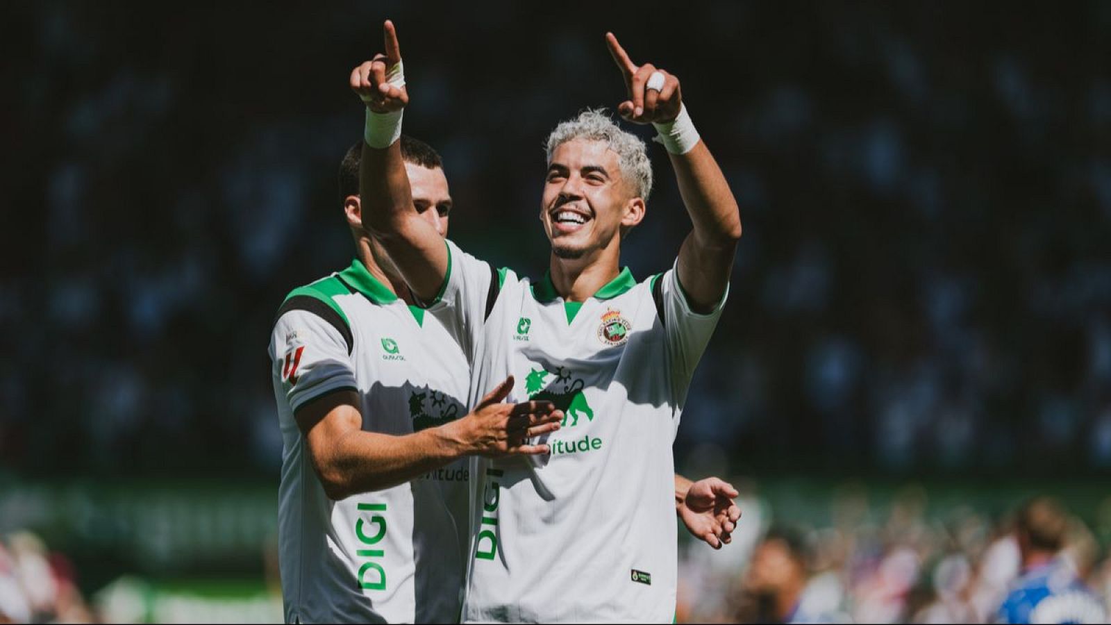 Aritz Zabala Astigarraga (Zabiri), con pelo rubio, celebra un gol con un compañero en un partido de fútbol. Ambos jugadores levantan sus brazos y sonríen, mostrando compañerismo.