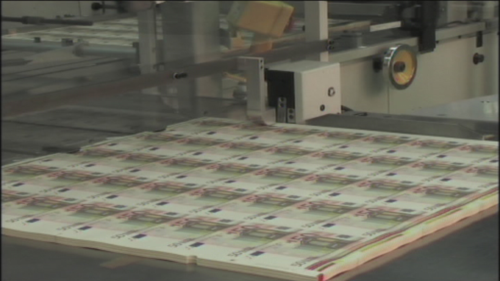 Hoja de billetes de 50 euros en proceso de producción, con maquinaria industrial al fondo.