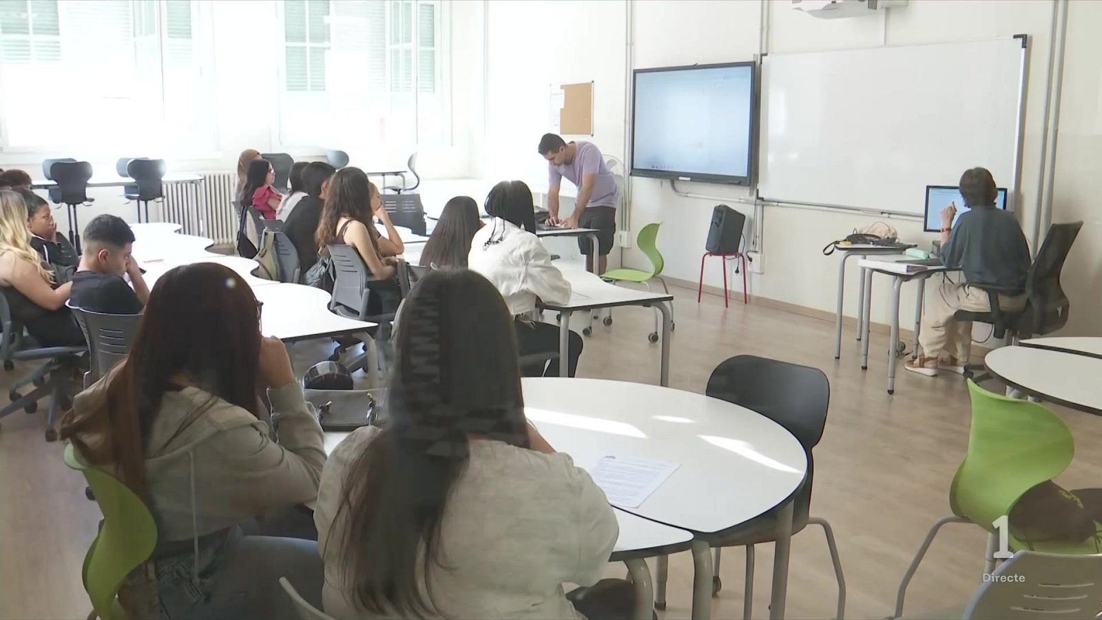 Jóvenes adultos en una sala de formación moderna con pantallas y portátiles. Captura de pantalla de "1 Directe".