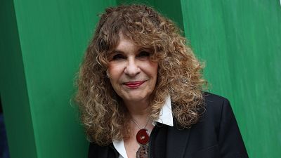 Massiel posa con un collar llamativo y pintalabios rojo, su cabello rizado enmarca su rostro. Fondo verde s�lido.