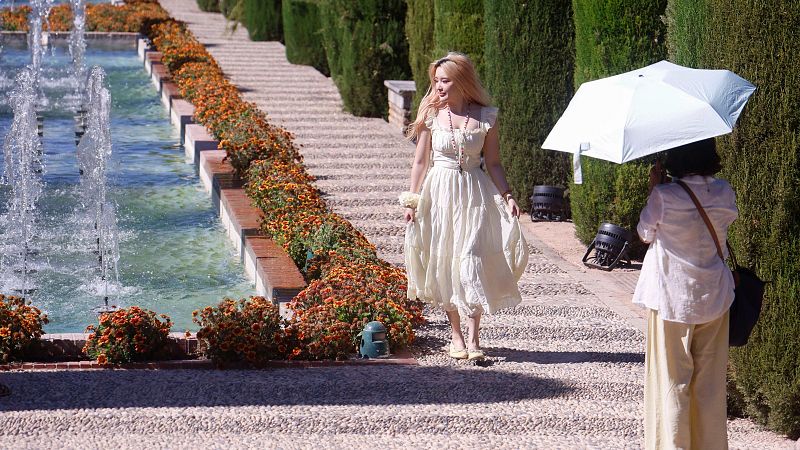 Turistas paseando con paraguas por las fuentes jardines del Alcázar de Córdoba para sofocar el intenso calor con temperaturas que llegan a los 38 grados
