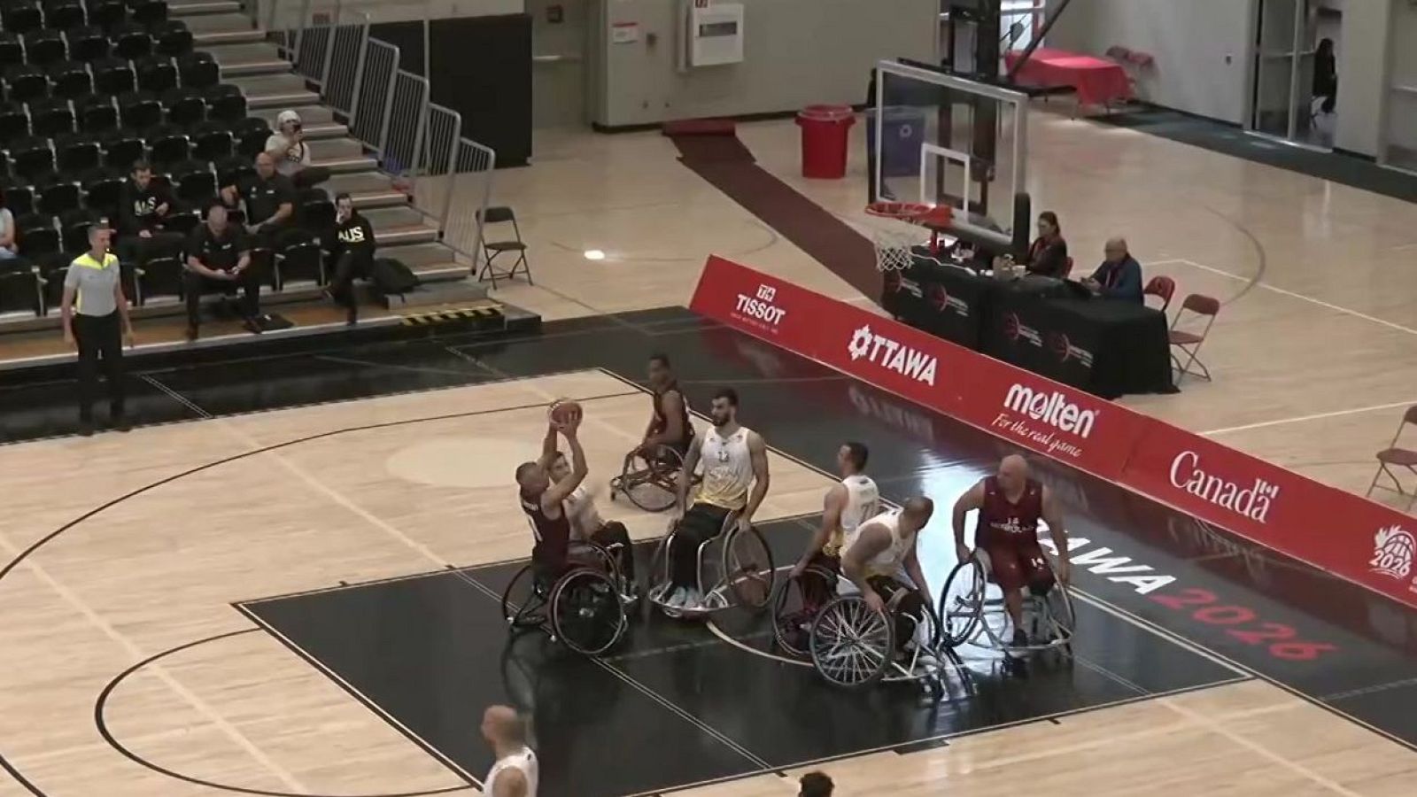 Jugador en silla de ruedas salta para lanzar el balón en un partido. Se ven patrocinadores como TISSOT y molten, y la indicación de Ottawa 2026.