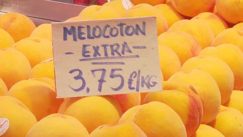 Primer plano de melocotones amarillos y anaranjados con un cartel que anuncia "MELOCOTON EXTRA-" a "3,75 €/KG".